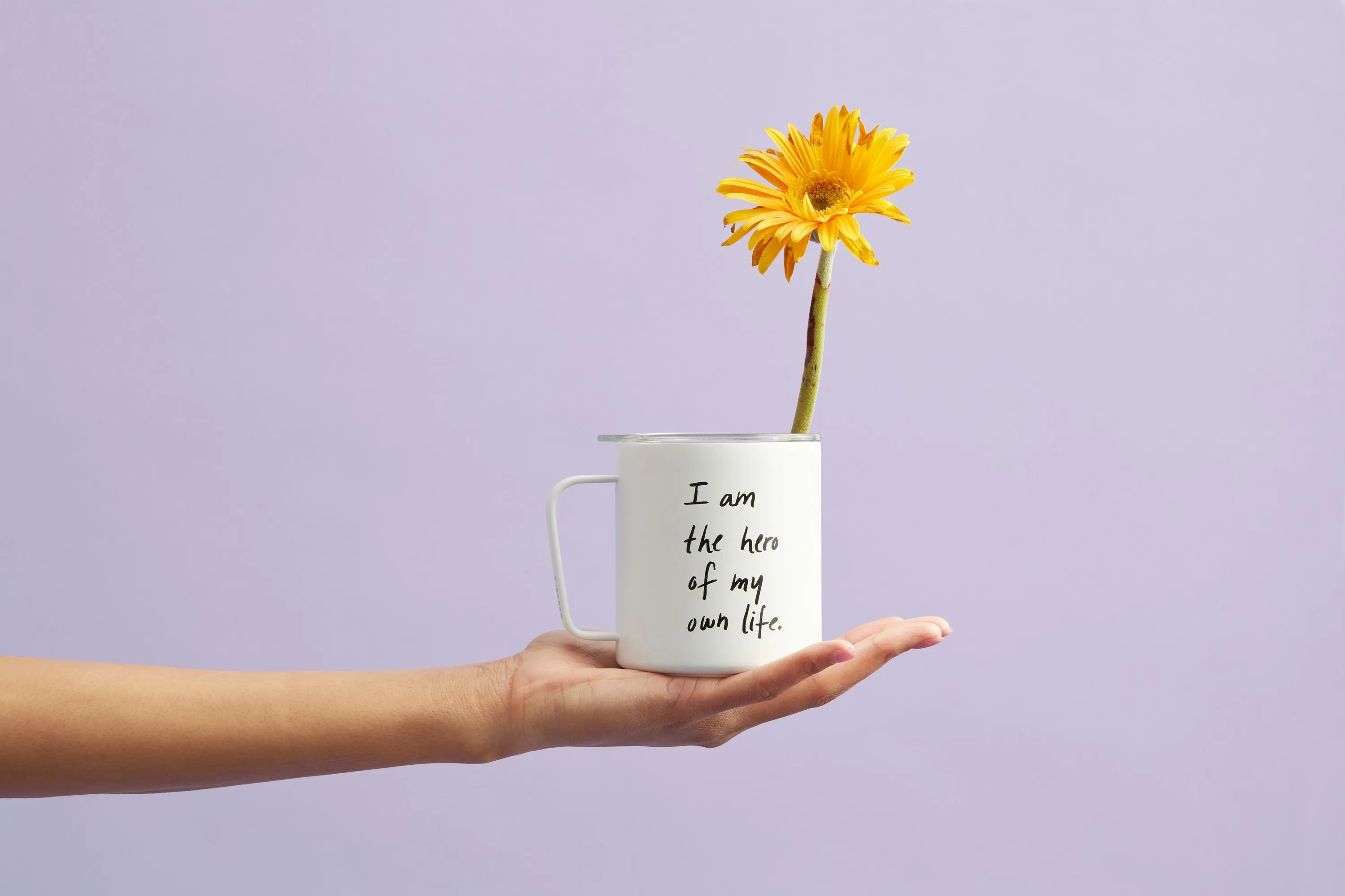 hand holding a cup with saying: I am my own hero