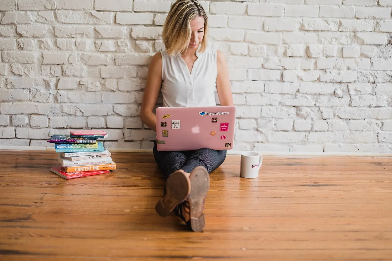 a female sitting on the floor writing on a laptop